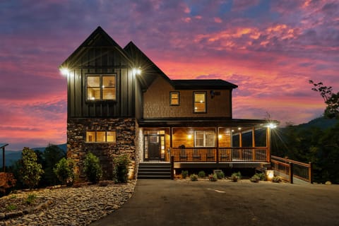 Two-story stone-and-wood cabin lit up at twilight under a pink and purple sunset sky