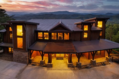Large timber-frame mountain lodge with a lit covered entrance at dusk