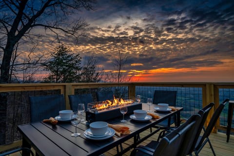 Outdoor dining table set for a meal beside a built-in fire feature overlooking a valley at sunset