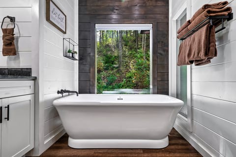 Freestanding soaking tub beneath a large window overlooking a wooded hillside