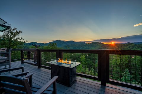 Deck fire pit table with adirondack chairs overlooking layered mountain ridges at sunset