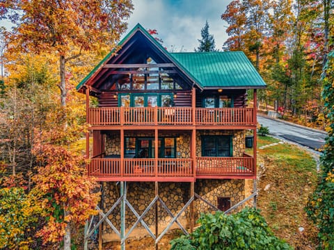 Three-story stone-and-log cabin with wraparound decks surrounded by peak fall foliage