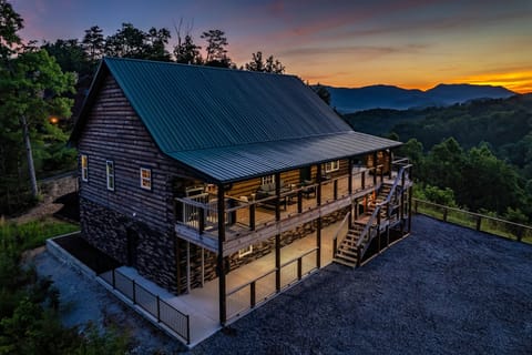Aerial view of a log cabin exterior at dusk with a covered deck and mountain view