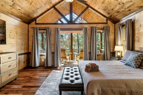 Vaulted-ceiling bedroom with a king bed and a private balcony overlooking the woods