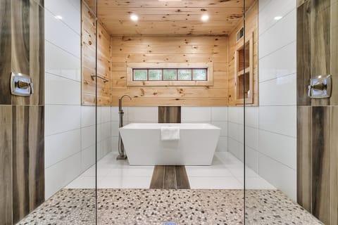 Freestanding soaking tub in a tiled bathroom viewed through a glass shower enclosure