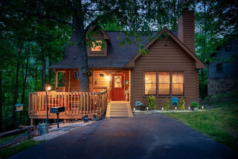 Wooded cabin with a red front door, covered deck, and glowing windows at twilight