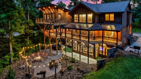 Multi-level cabin lit at twilight with tiered decks, a fire pit patio, and string lights